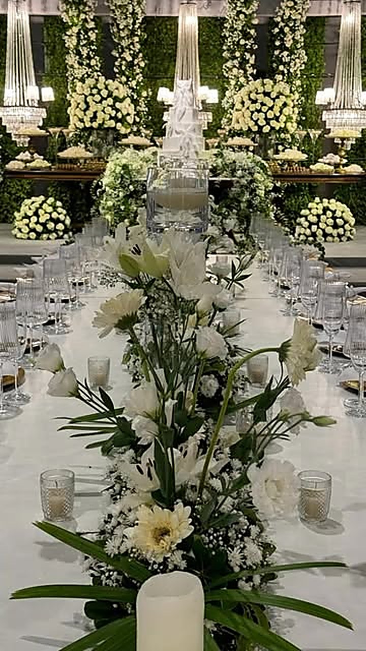 Mesa de jantar com arranjo alto de flores brancas, velas e taças